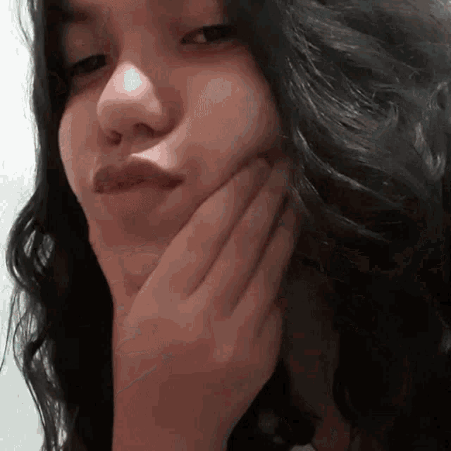 a woman with long black hair is making a funny face with her hand on her chin
