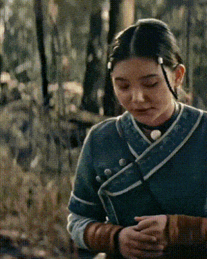 a woman in a green and blue outfit is standing in a forest