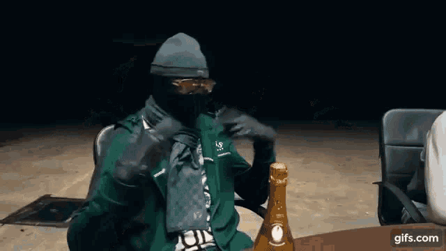 a man wearing a mask is sitting at a table with a bottle of champagne