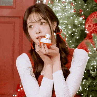 a woman holds a cupcake with a snowman on it in front of a christmas tree