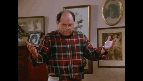a man in a plaid shirt is standing in a living room holding his hands out .