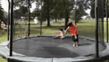 two children are playing on a round trampoline in a park