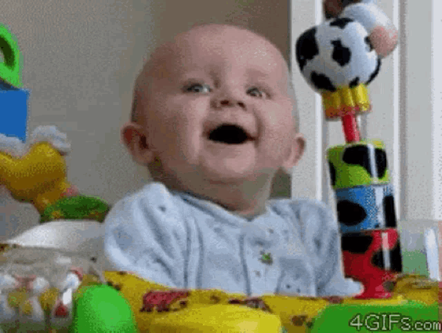 a baby is sitting in a crib with toys and smiling with his mouth open .