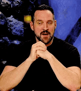 a man with a beard and mustache is sitting with his hands folded