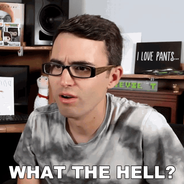 a man wearing glasses says " what the hell " in front of a sign that says " i love pants "