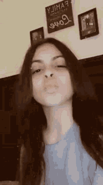 a young woman with long hair is making a funny face in front of a wall with pictures on it .