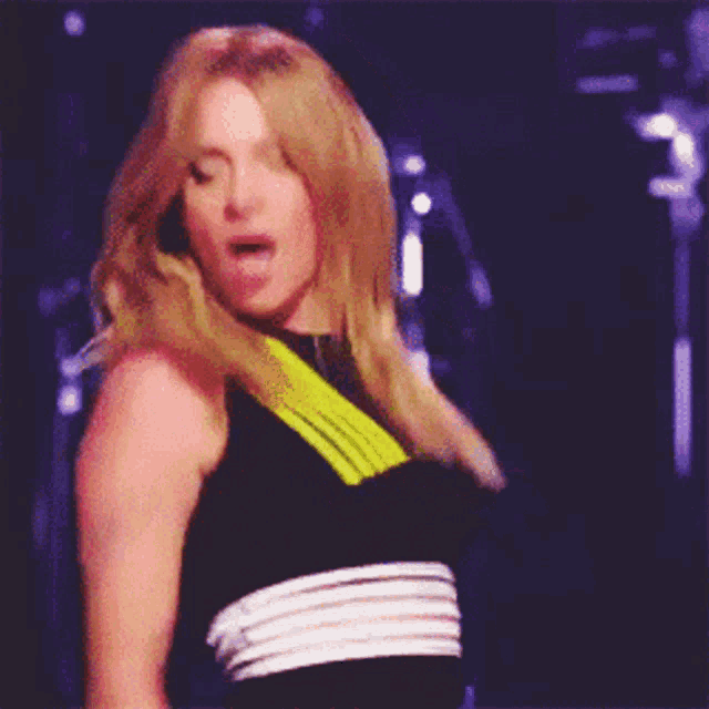 a woman in a black and yellow top is dancing on a stage