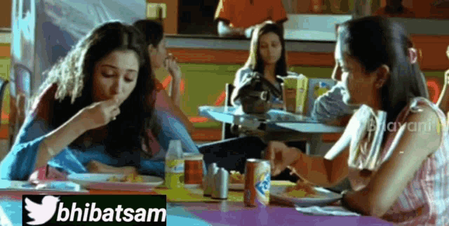 two women are sitting at a table eating food with a twitter logo in the upper right corner