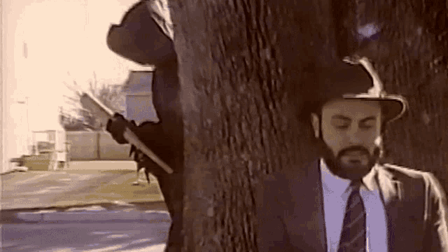 a man in a suit and tie is standing under a tree