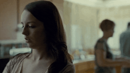 a woman is sitting in a room with a man and a woman standing in the background .