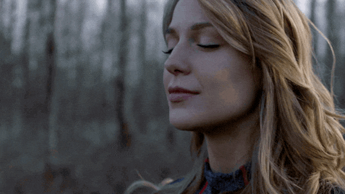 a woman with her eyes closed stands in the woods