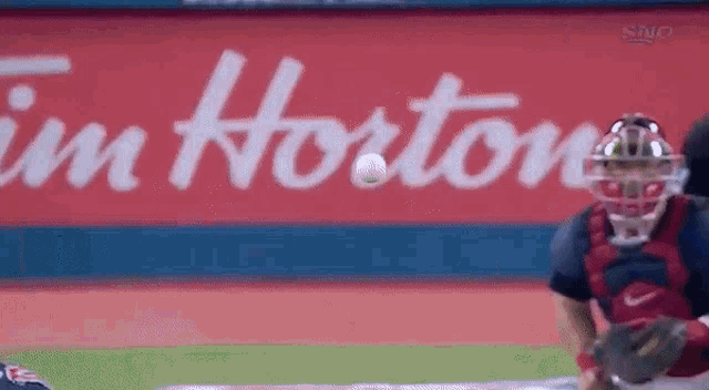 a catcher catches a ball in front of a tim hortons sign