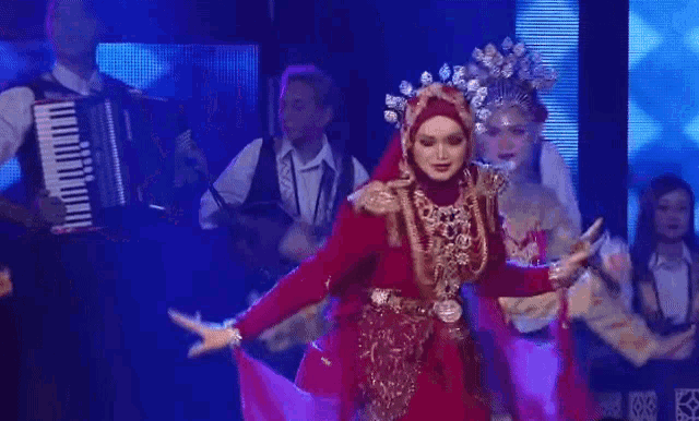 a woman in a red dress is dancing on a stage with a man playing an accordion behind her .