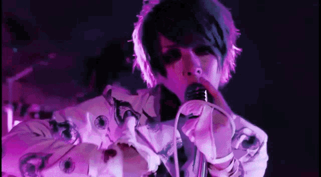 a person is singing into a microphone while wearing a purple shirt .