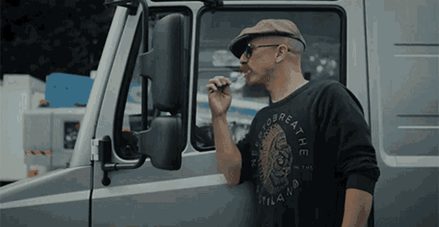 a man smoking a cigarette in front of a truck wearing a shirt that says " no breath "