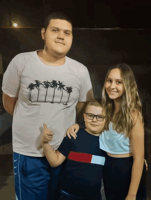 a boy wearing a white shirt with palm trees on it poses for a picture with two other kids