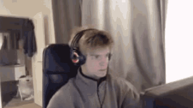 a young man wearing headphones is sitting in a chair in front of a computer screen .