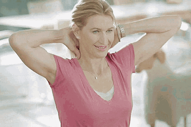 a woman in a pink shirt is smiling and stretching her arms