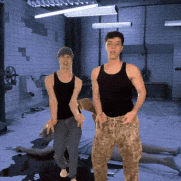 two men in black tank tops are standing in a room with a dead body on the floor