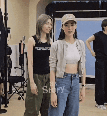 two women are standing next to each other in a room and one of them is wearing a baseball cap .
