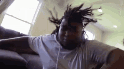 a man with dreadlocks is sitting on a couch in a living room with his hair blowing in the wind .