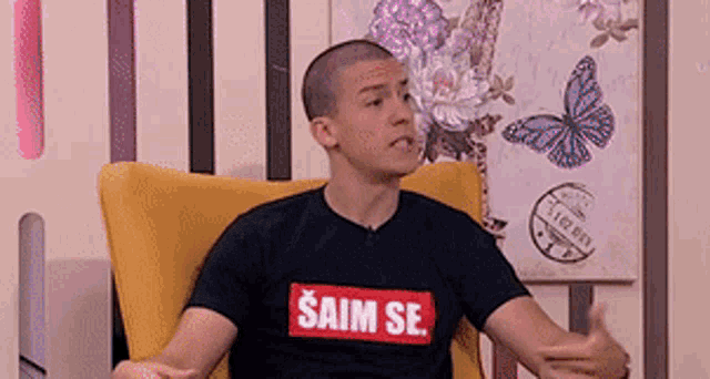a young man is sitting in a yellow chair wearing a black shirt that says ' saim se ' on it .