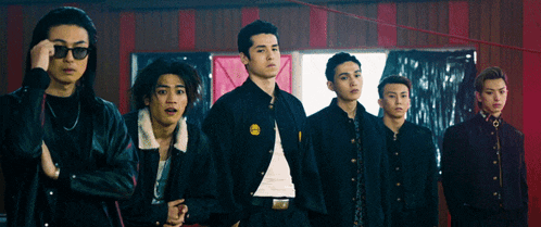 a group of young men are standing in a row with one wearing a jacket with a yellow smiley face on it