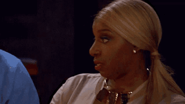 a woman with blonde hair is wearing a white shirt and gold necklace