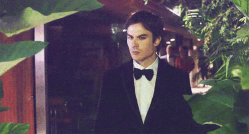 a man in a tuxedo and bow tie is standing in a dark room