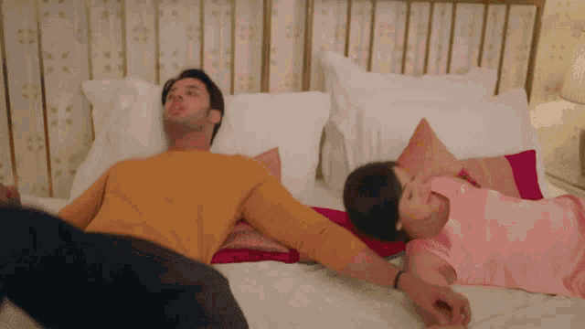 a man in a yellow shirt is laying on a bed next to a woman in a pink dress