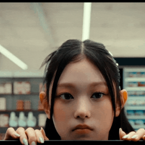 a close up of a young girl 's face with her hands on a shelf