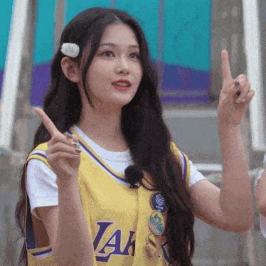 a girl wearing a yellow lakers jersey points up