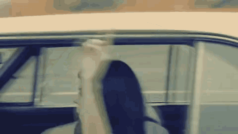 a woman is sitting in a car looking out the window and waving her hand .
