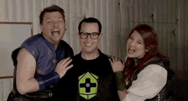 two men and a woman are posing for a picture and the man is wearing a shirt with a green cross on it