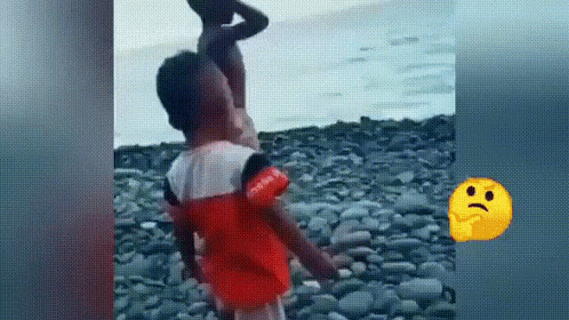 a boy is holding another boy on his shoulders on a rocky beach .