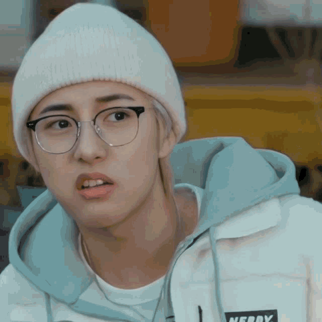 a young man wearing glasses and a white beanie has a nerdy logo on his jacket