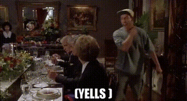 a group of people are sitting at a table with a man standing behind them and the words yells written on the screen .