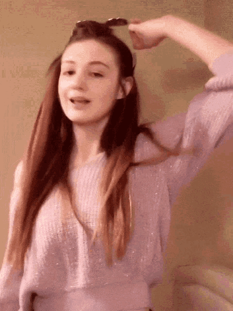 a girl wearing a purple sweater is holding a pair of sunglasses on her head