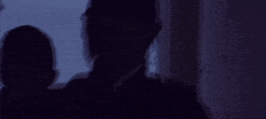 a man in a white shirt and tie is sitting in a dark room with his head down .