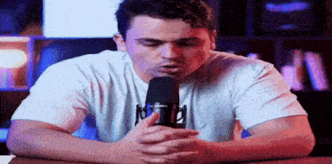 a man in a white t-shirt is singing into a microphone with the letter r on it