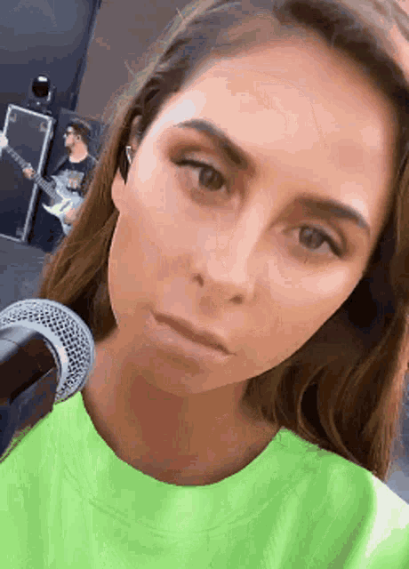 a woman in a neon green shirt is taking a selfie with a microphone in front of her