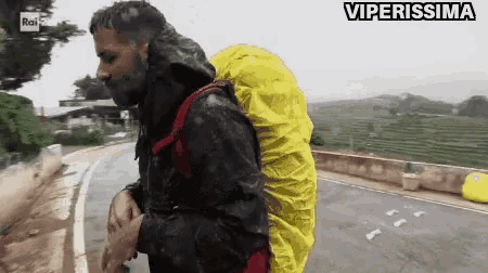 a man with a yellow backpack is walking down a road with the words viperissima written above him
