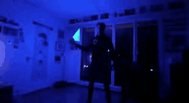 a person is standing in a dark room with a blue light behind them .