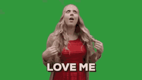 a woman in a red dress is holding her hair in front of a green screen and saying `` love me '' .