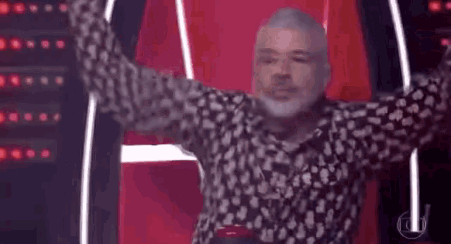 a man with a beard is sitting in a chair with his arms outstretched in front of a red wall .
