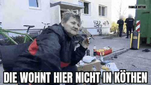a woman is sitting on the side of the road smoking a cigarette in front of a building .