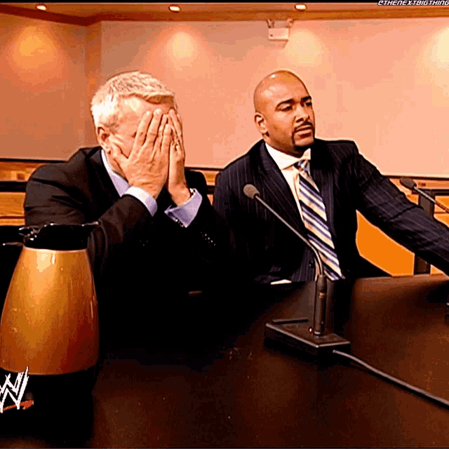 two men are sitting at a table with a wwe logo on it