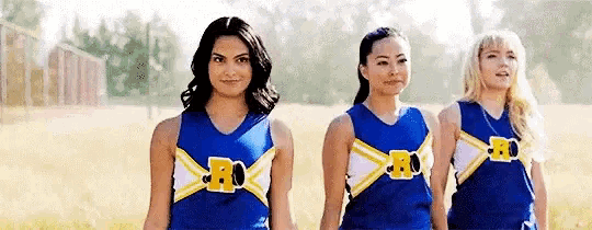 three cheerleaders are standing next to each other in a field wearing blue uniforms .