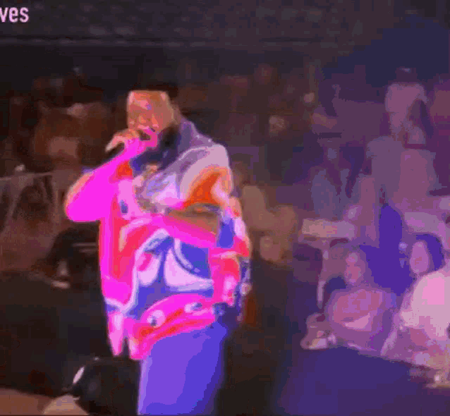a man in a colorful shirt is singing into a microphone in front of a crowd with the word ves in the corner