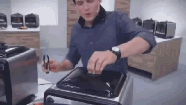 a man in a blue shirt is holding a pair of tweezers over a stove top oven .